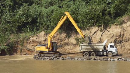 Hydraulikbagger und Kipper LKW bei Arbeiten zur Flussuferbefestigung