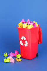 Recycling bin with papers on blue background