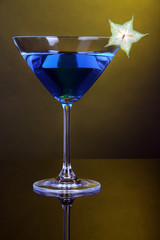 Blue cocktail in martini glass on dark yellow background