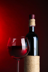 Glass of wine with bottle on bright red background