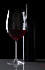 Naklejka na ściany i meble Glass of wine with bottle on black background