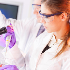 Young scientist pipetting red solution.