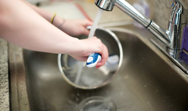 Woman washes metal bowl in kitchen sink