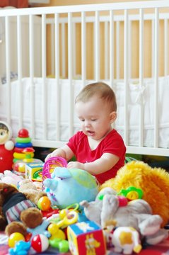 baby plays toys against white bed