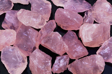 Closeup picture of many rough rose quartz gems on the black.