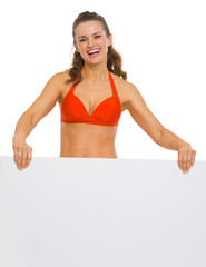 Happy young woman in swimsuit showing blank billboard