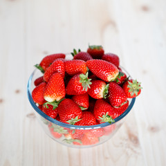 Strawberries in a glass bowl on a wooden table, square