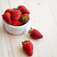 Strawberries in a white cocotte on a wooden table, square