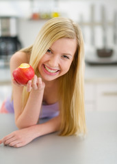 Happy teenager girl eating apple in kitchen