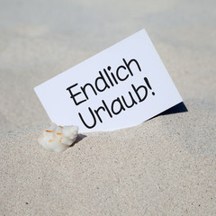 Muschel im Sand mit Karte ENDLICH URLAUB