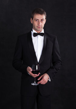Stylish man in elegant black tuxedo with glass red wine