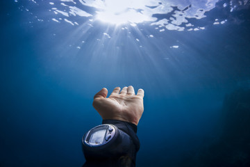 Scuba divers hand reaching out to sun light on blue background