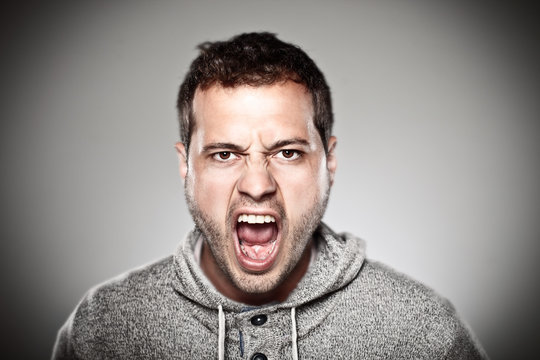 Young man screaming over grey background.