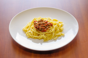 Fettuccine or tagliatelle with bolognese sauce, also called ragu, in a white plate on a wooden table