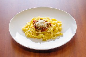 Fettuccine or tagliatelle with bolognese sauce, also called ragu, with parmesan, in a white plate on a wooden table