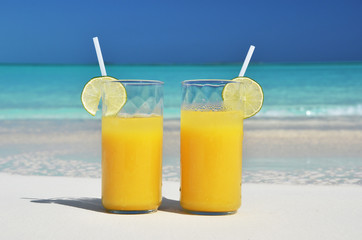 Two glasses of orange juice on the sandy beach