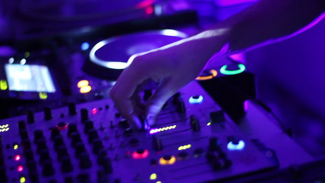 DJ hands tweak controls on turntable record deck in night club.