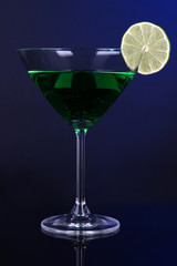 Green cocktail in martini glass on dark blue background