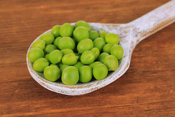 Sweet green peas in spoon on wooden background