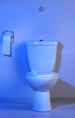 Toilet bowl and toilet paper in a bathroom with blue light
