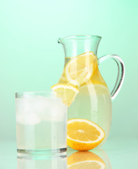 Lemonade in pitcher and glass on green background