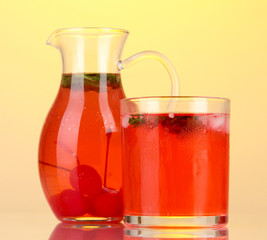 Cherry drink in pitcher and glass on yellow background.