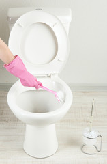 Woman hand with brush cleaning a toilet bowl in a bathroom