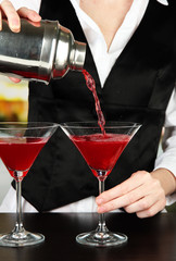 Barmen hand with shaker  pouring cocktail into glasses,