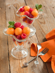 Fruit salad with melon balls and raspberries in glass bowl