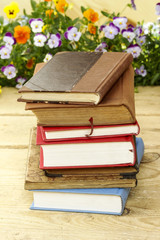 Pile of books on wooden vintage table, fresh blooming flowers in