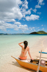 portrait of slim young bikini girl sitting on tip of beach boat