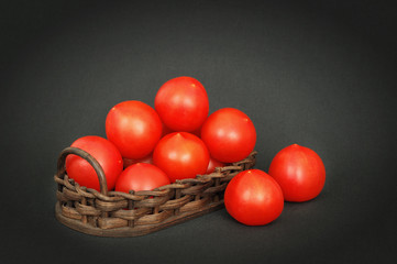 Little red tomatoes in a basket on dark table