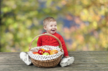 baby with basket of apples, seated on a old wooden table