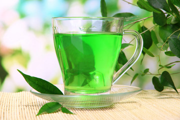 Transparent cup of green tea on bamboo mat, on nature