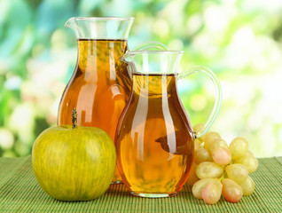 Apple juice in pitchers on table on bright background