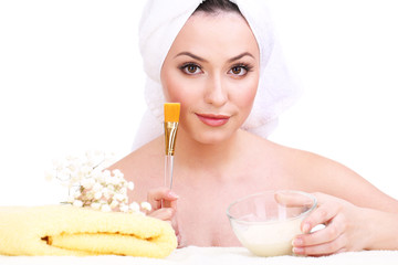 Beautiful young woman with cream for face mask and towel