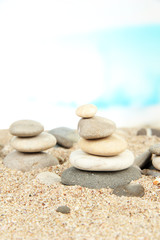 Fototapeta na wymiar Tower of sea stones on sand on bright background