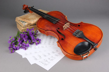 Fototapeta premium Classic wooden violin with sheet music, vintage books, and purple flowers on gray background