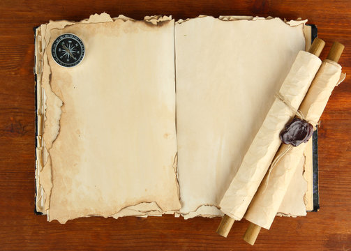 Open old book, scrolls and compass on wooden background