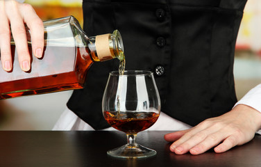 Barman hand with bottle of cognac  pouring drink into glass,