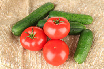 Tasty green cucumbers and red tomatoes on sackcloth background