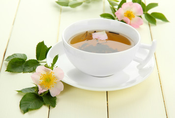 Cup of herbal tea with hip rose flowers on white wooden table