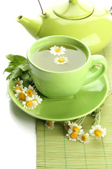 Cup and teapot of herbal tea with wild camomiles and mint,