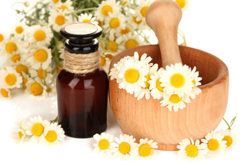 Essential oil and chamomile flowers in mortar close up