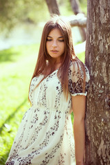 Girl in a summer dress leaning on an old tree