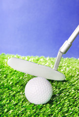 Golf ball and club on green field grass against blue sky