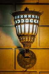 Glowing antique wall lamp with shades patterns on the wall.