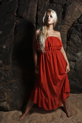 Beautiful blond woman in red dress near the rock