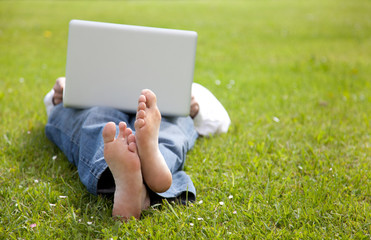 Hombre tumbado en la hierba consultando el portatil