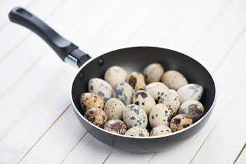 Frying pan with raw quail eggs on wooden boards